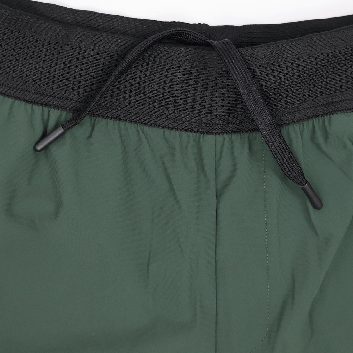 Close-up of the waistband of green Canterbury Everest Woven Short 5" athletic shorts, featuring a black elastic band and center-tied drawstring. Made from four-way stretch fabric for comfort during training. Brand: Canterbury.