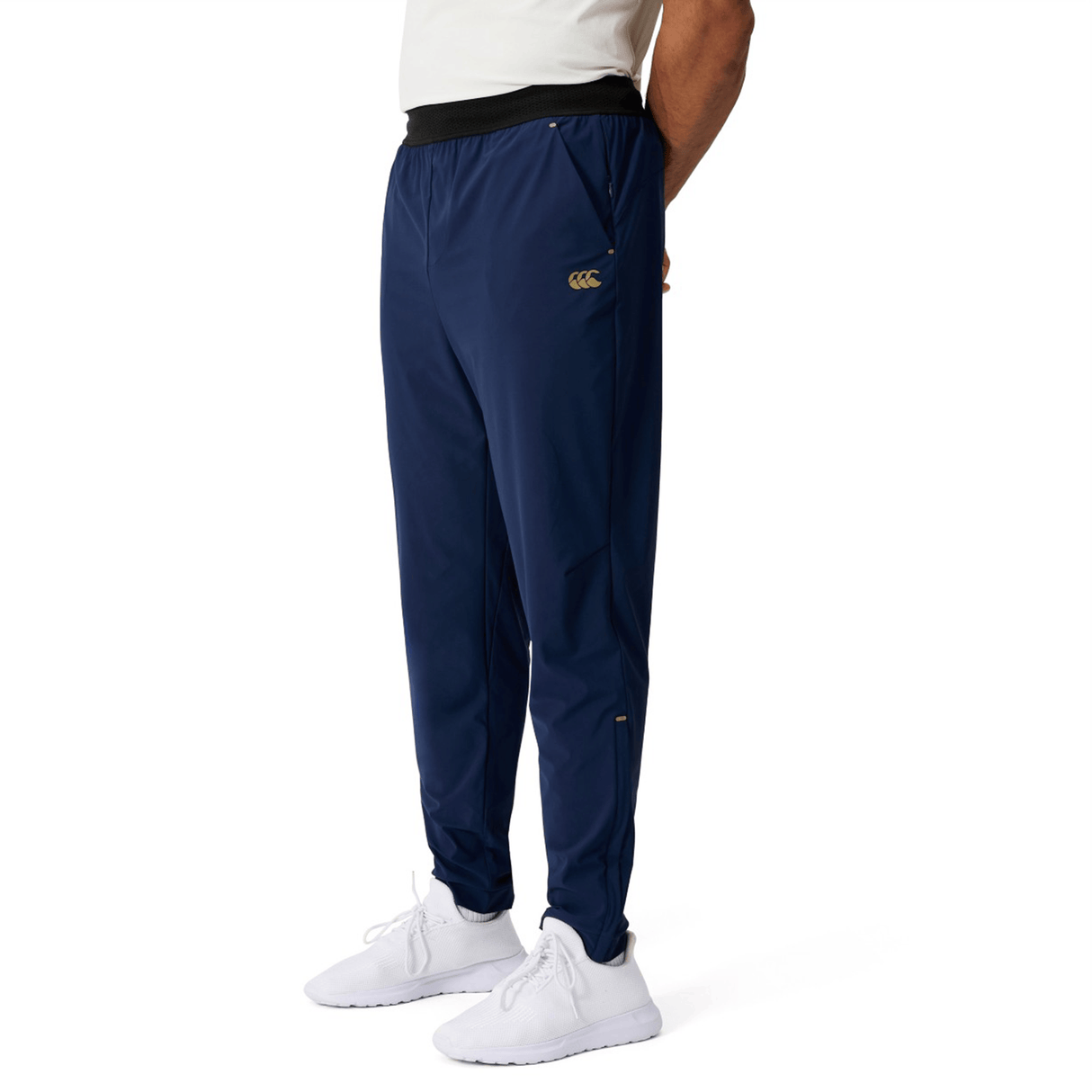 A person wearing Canterbury Everest Woven Pant 30" in navy blue, paired with a white shirt and white sneakers, stands against a plain white background.