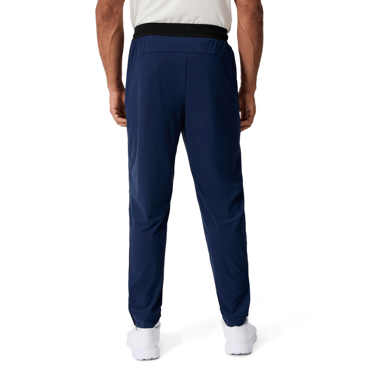 A man wearing Canterbury Everest Woven Pant 30" in navy blue, with a white shirt and white shoes, stands with his back to the camera against a plain white background.