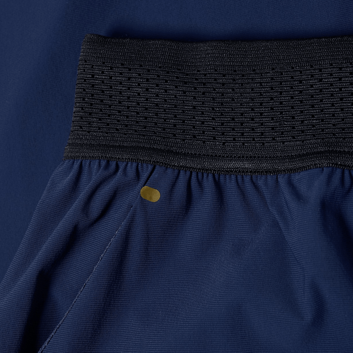 Close-up of the Canterbury Everest Woven Pant 30" in blue, highlighting its black elastic waistband, sweat-wicking four-way stretch fabric, and a small gold circular detail near the seam.