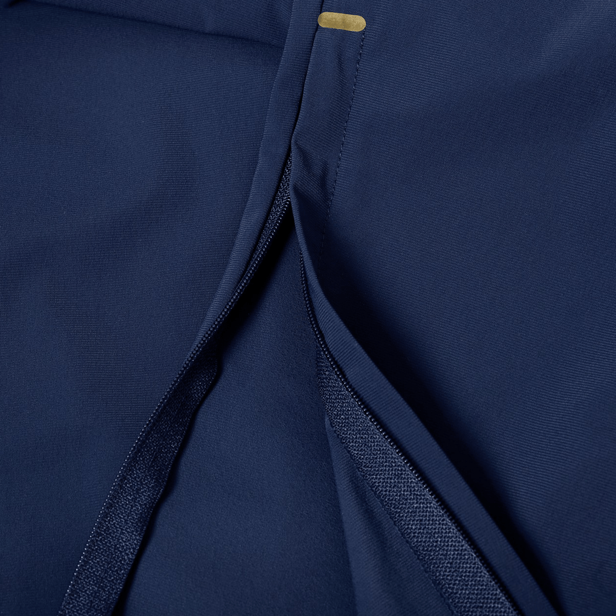 Close-up of the Canterbury Everest Woven Pant 30" by Canterbury in navy, showing a partially open seam with reinforced stitching, sweat-wicking fabric, and a small gold rectangular accent near the top edge.