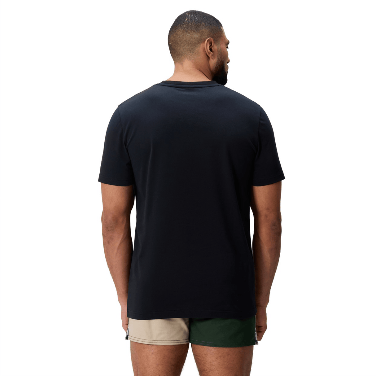 A man stands with his back to the camera, wearing a Canterbury FUN. T-SHIRT AM and two-tone shorts—beige on one side, green on the other.