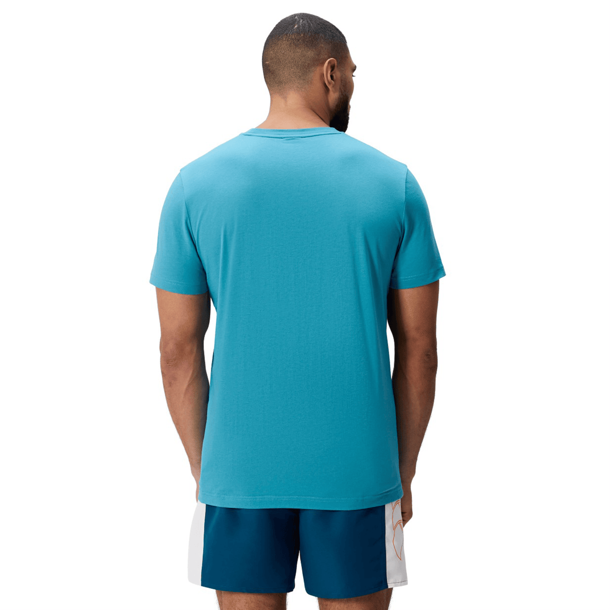 A man stands with his back to the camera, wearing a Canterbury FUN. T-SHIRT AM in teal and blue athletic shorts against a white background.