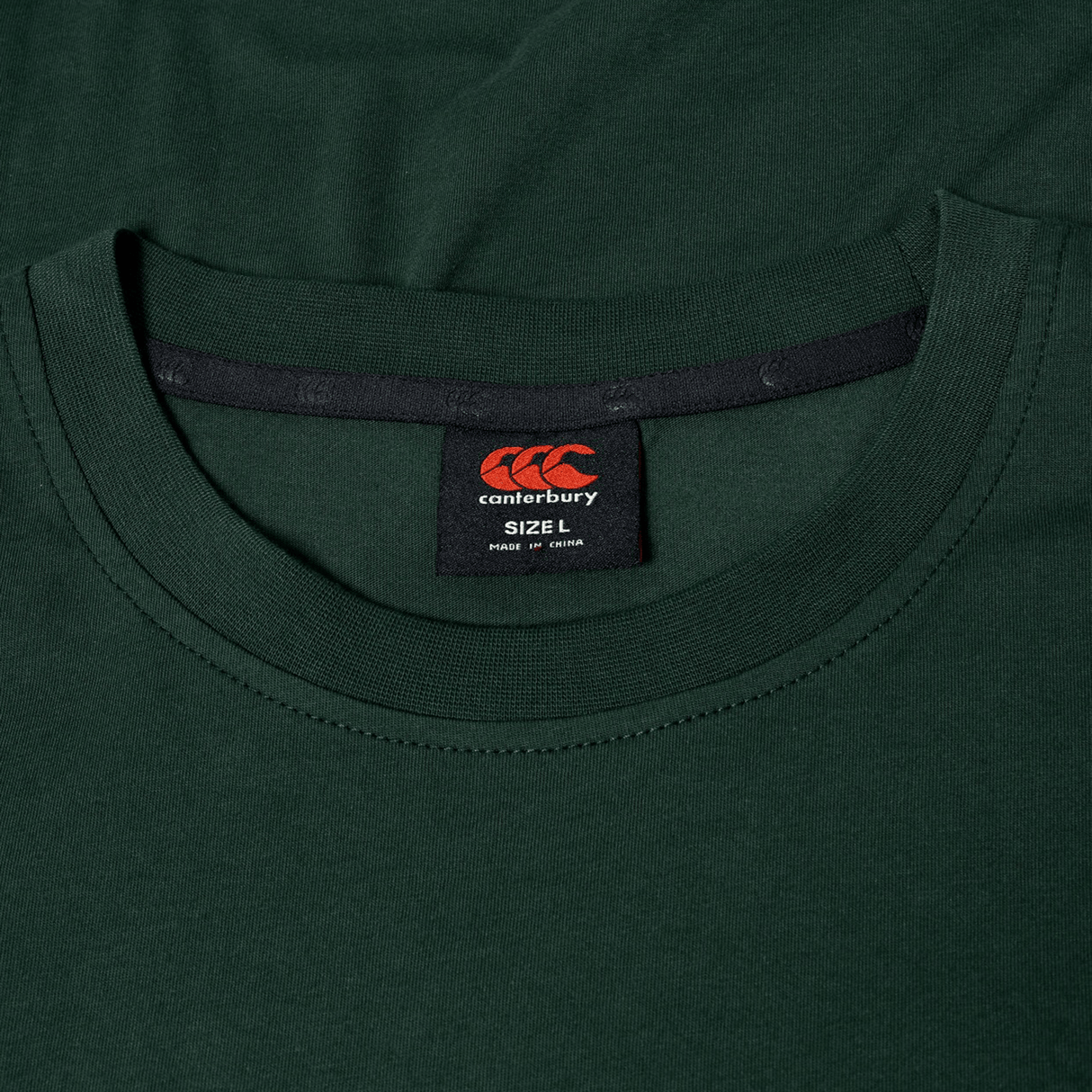 Close-up of a dark green Canterbury FUN. T-SHIRT AM, focusing on the collar and inside label showing size L and made in China.