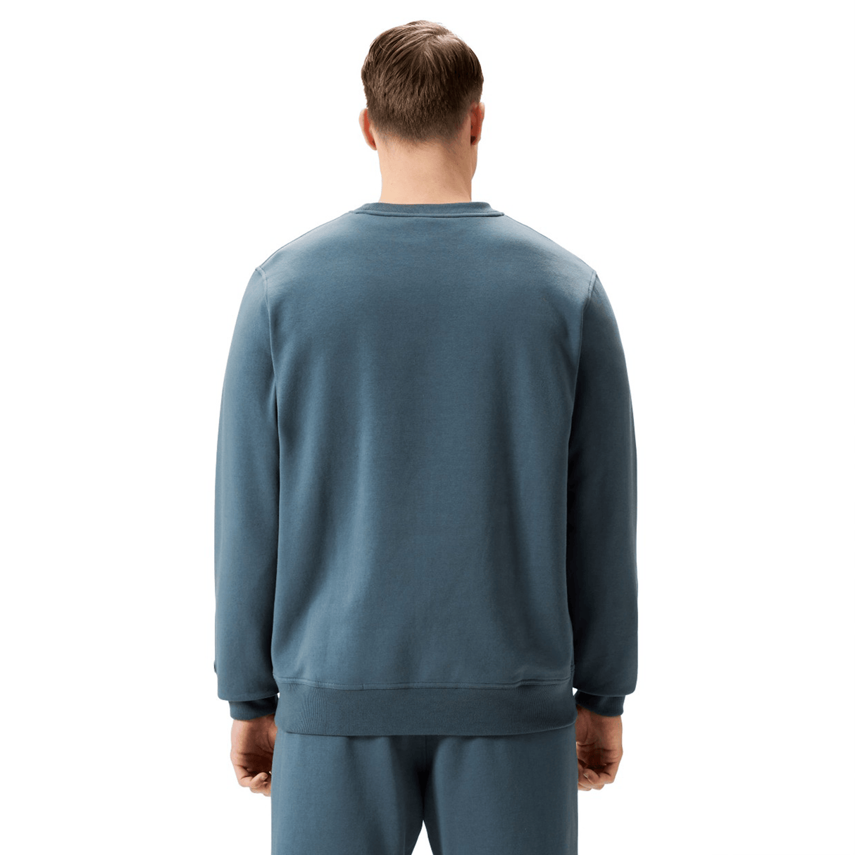 A man stands with his back to the camera, wearing a blue Canterbury EVERYDAY GFX CREW SWEATER and matching pants, ideal for daily wear, set against a plain white background.