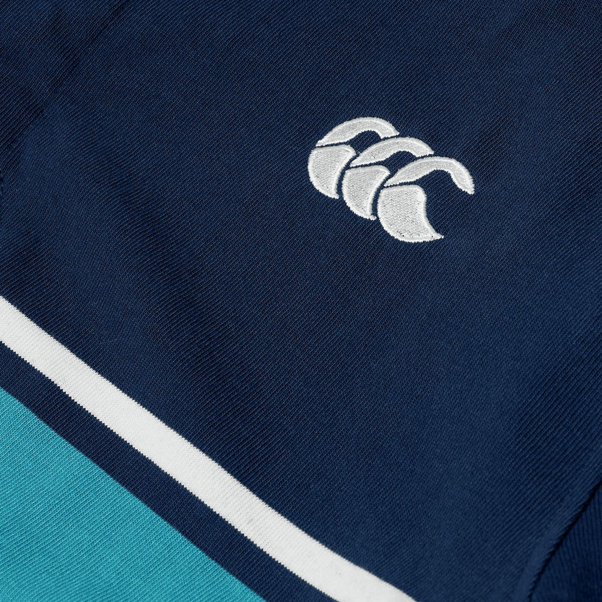 Close-up of the Canterbury Stripe Rugby Jersey by Canterbury in navy blue, showcasing a white embroidered logo with three overlapping curves and two horizontal stripes in white and turquoise.