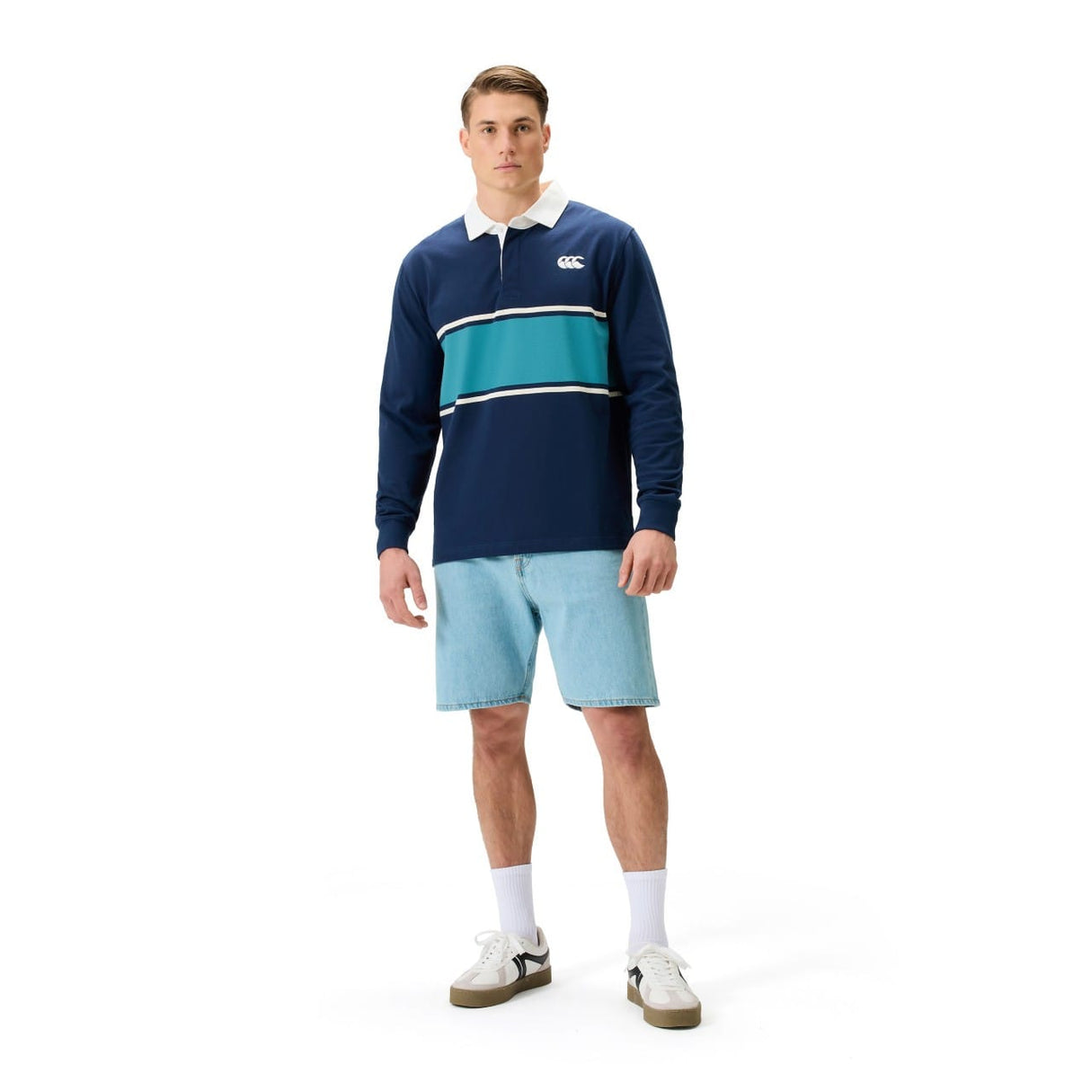 A man faces the camera wearing a Canterbury Stripe Rugby Jersey by Canterbury, paired with light blue denim shorts, white socks, and white sneakers.