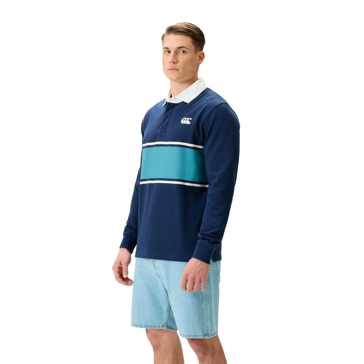 A man stands against a white background wearing the Canterbury Stripe Rugby Jersey and light blue denim shorts.