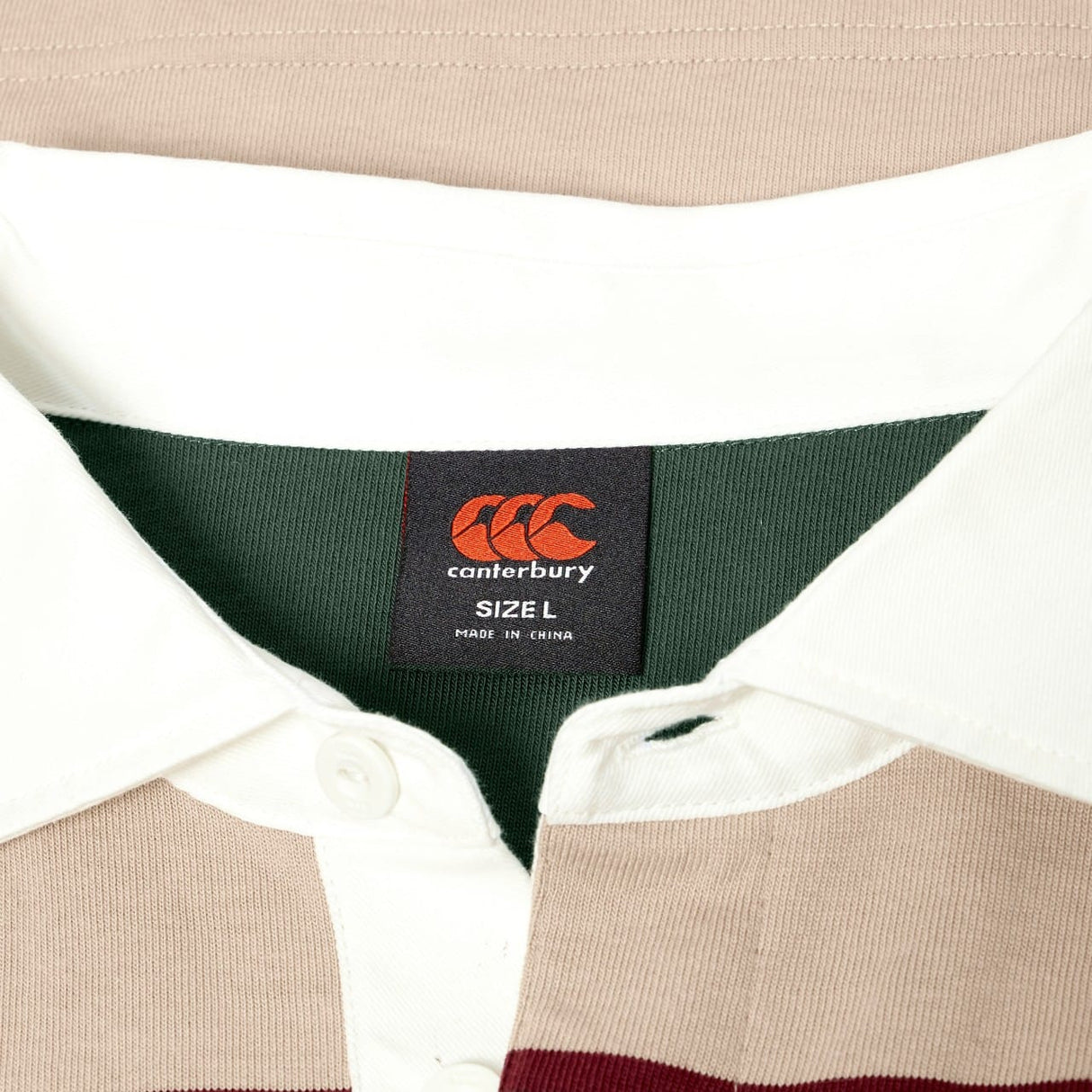 Close-up of a Canterbury Stripe Rugby Jersey collar, displaying the Canterbury logo label (size L, Made in China). The shirt showcases beige, white, and green stripes in a classic rugby design.