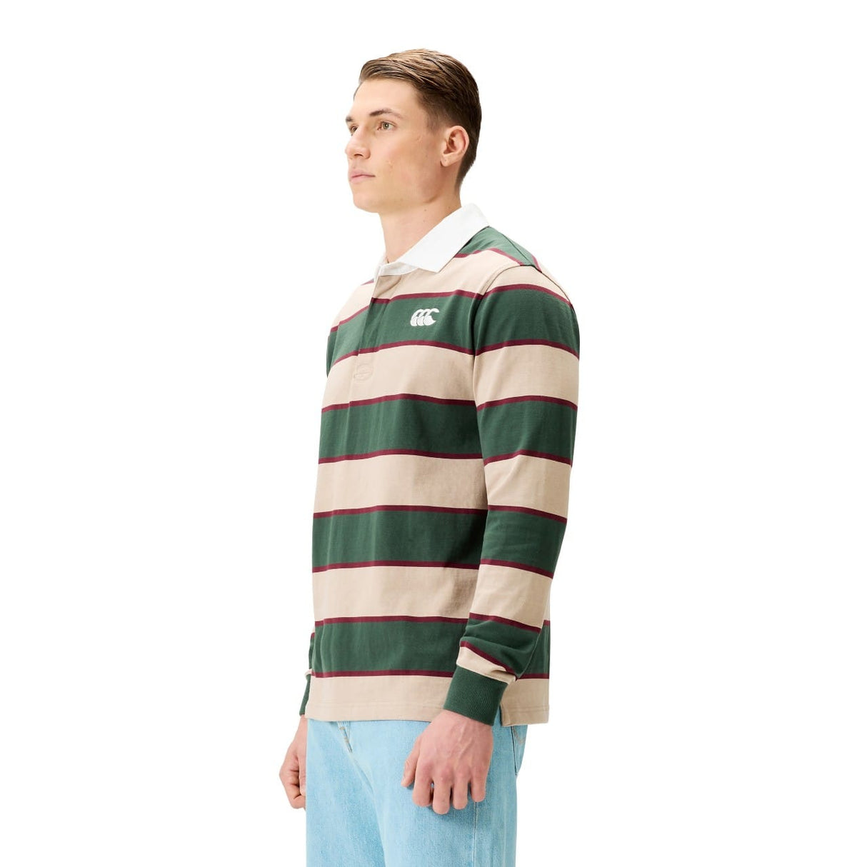 A man stands against a white background wearing the Canterbury Stripe Rugby Jersey by Canterbury, featuring green, beige, and red stripes with a white collar, paired with light blue jeans.