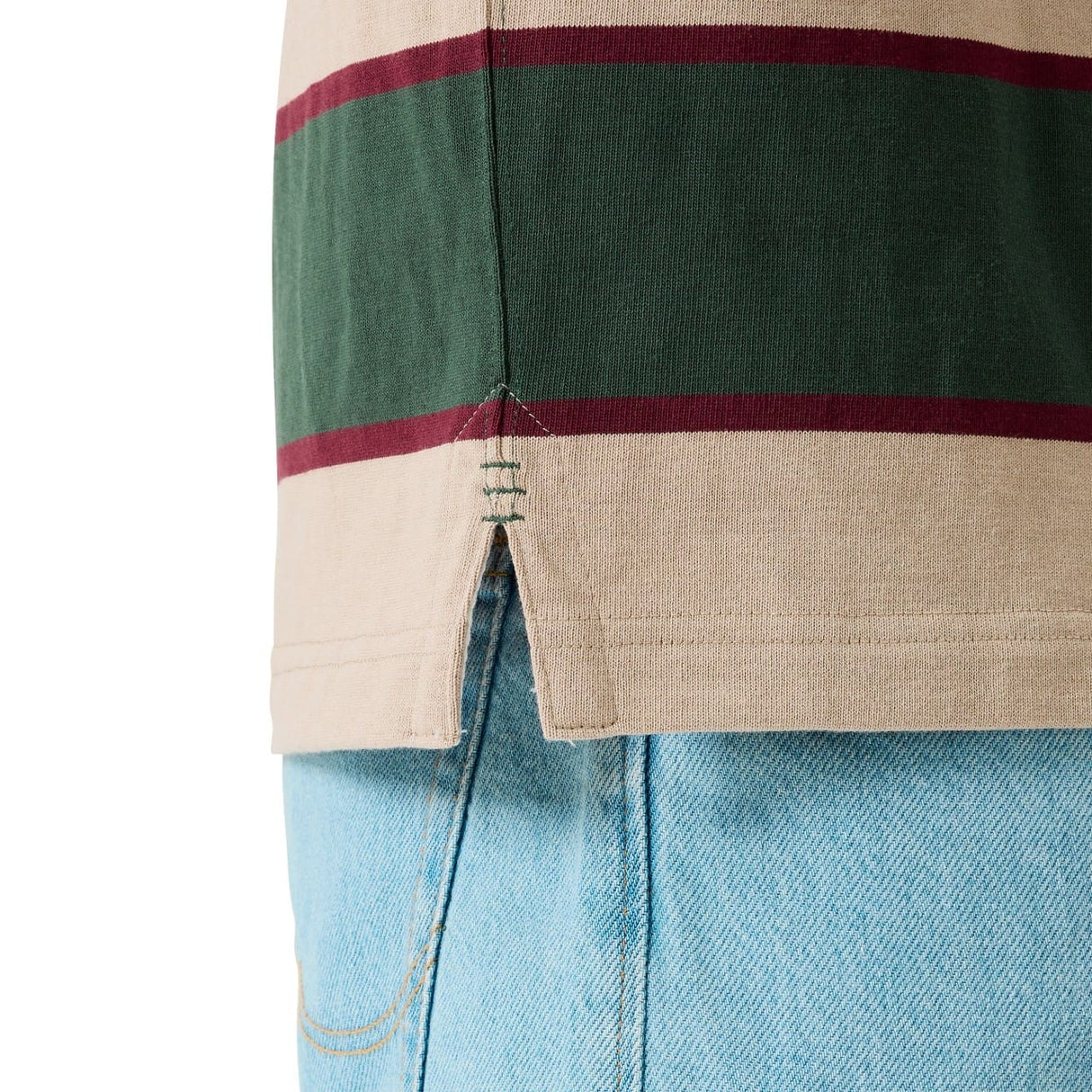 Close-up of the Canterbury Stripe Rugby Jersey by Canterbury in beige, green, and maroon with a side slit hem, styled over light blue denim jeans.