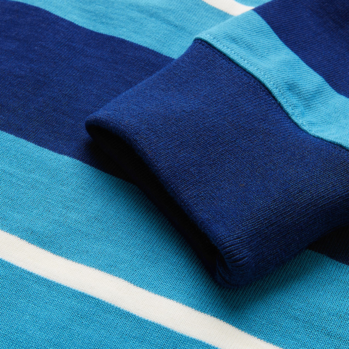 Close-up of a sleeve and fabric on the Canterbury Stripe Classic Rugby Jersey by Canterbury, highlighting wide blue stripes, a thin white stripe, and durable cotton blend knit.