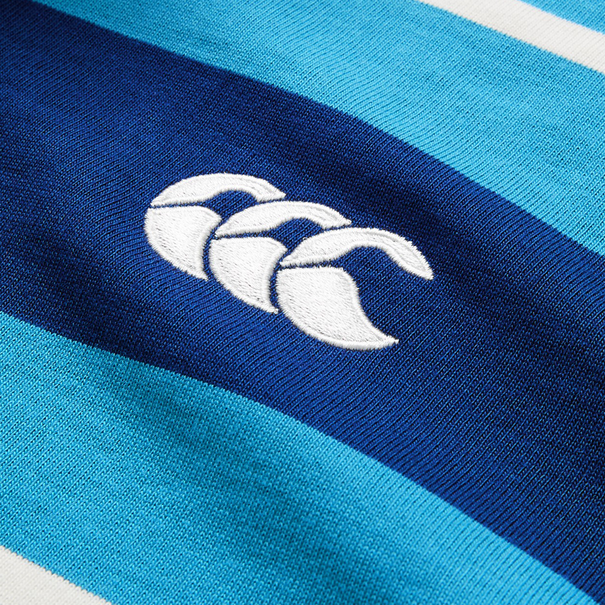 Close-up of the Canterbury Stripe Rugby Jersey by Canterbury in blue, featuring a white embroidered logo and classic rugby shirt styling.