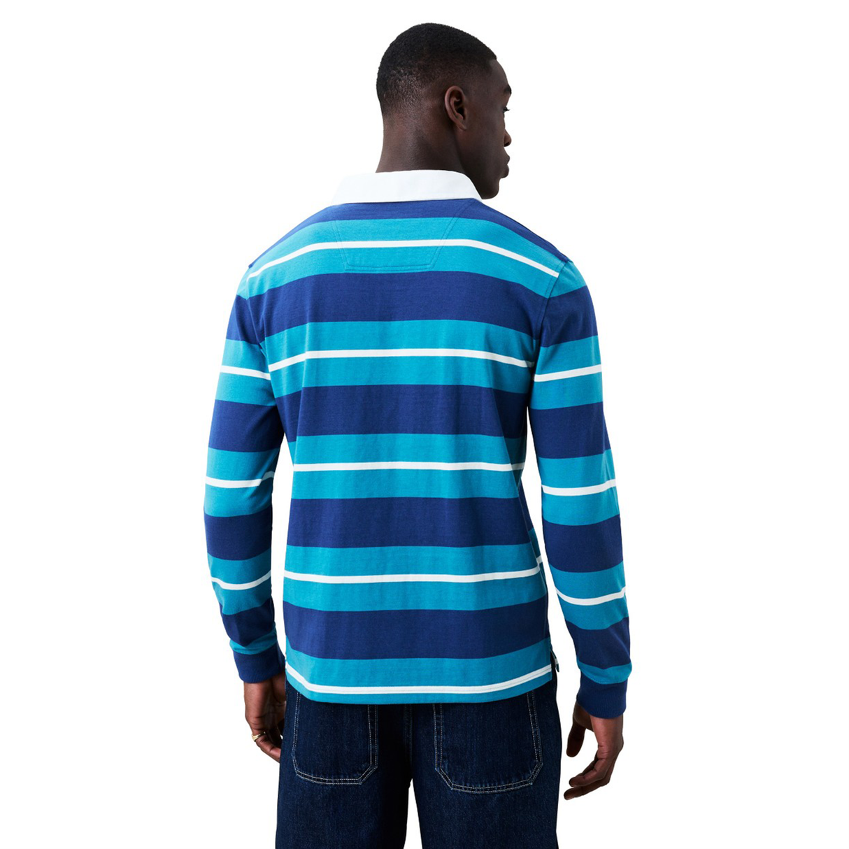 A person stands facing away, wearing the Canterbury Stripe Classic Rugby Jersey by Canterbury—a long-sleeve, blue and turquoise striped cotton-blend jersey with a white collar—paired with dark denim jeans against a plain white background.