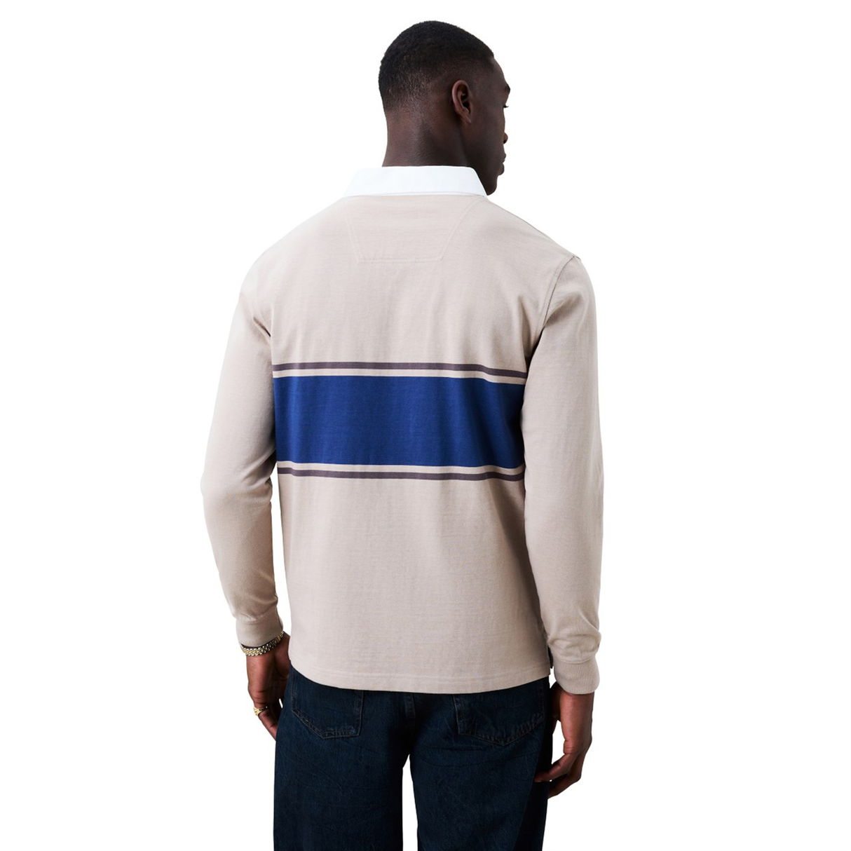 A man, seen from behind, wears the Canterbury Stripe Classic Rugby Jersey by Canterbury—beige with a blue back stripe, made from a durable cotton blend—paired with dark jeans against a plain white background.
