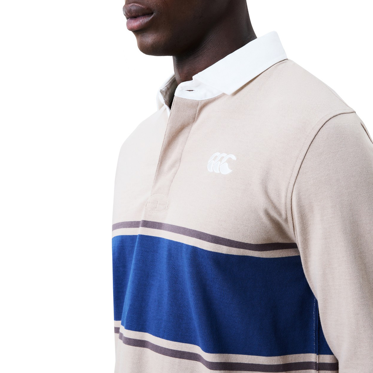 A person wears the Canterbury Stripe Classic Rugby Jersey by Canterbury, featuring navy and khaki stripes, a white collar, durable cotton blend fabric, and a white embroidered chest logo.