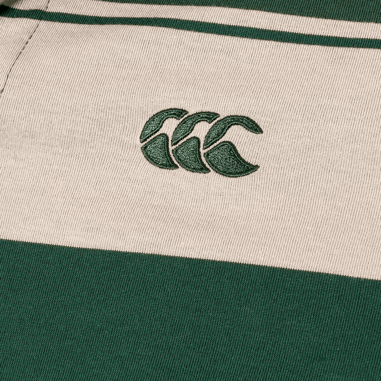 Close-up of Canterbury Yarn Stripe Polo fabric by Canterbury, featuring green and beige stripes and an embroidered logo with three overlapping green curves, showcasing classic rugby style.