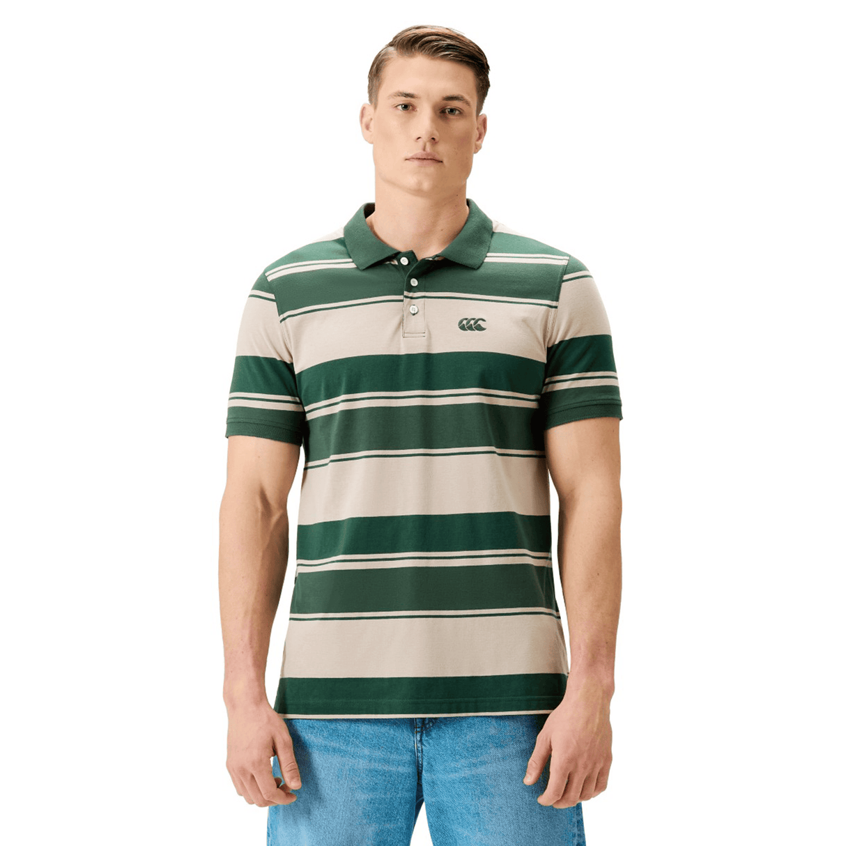 A man in a green and beige Canterbury Yarn Stripe Polo by Canterbury, featuring classic rugby style, pairs it with blue jeans against a white background.