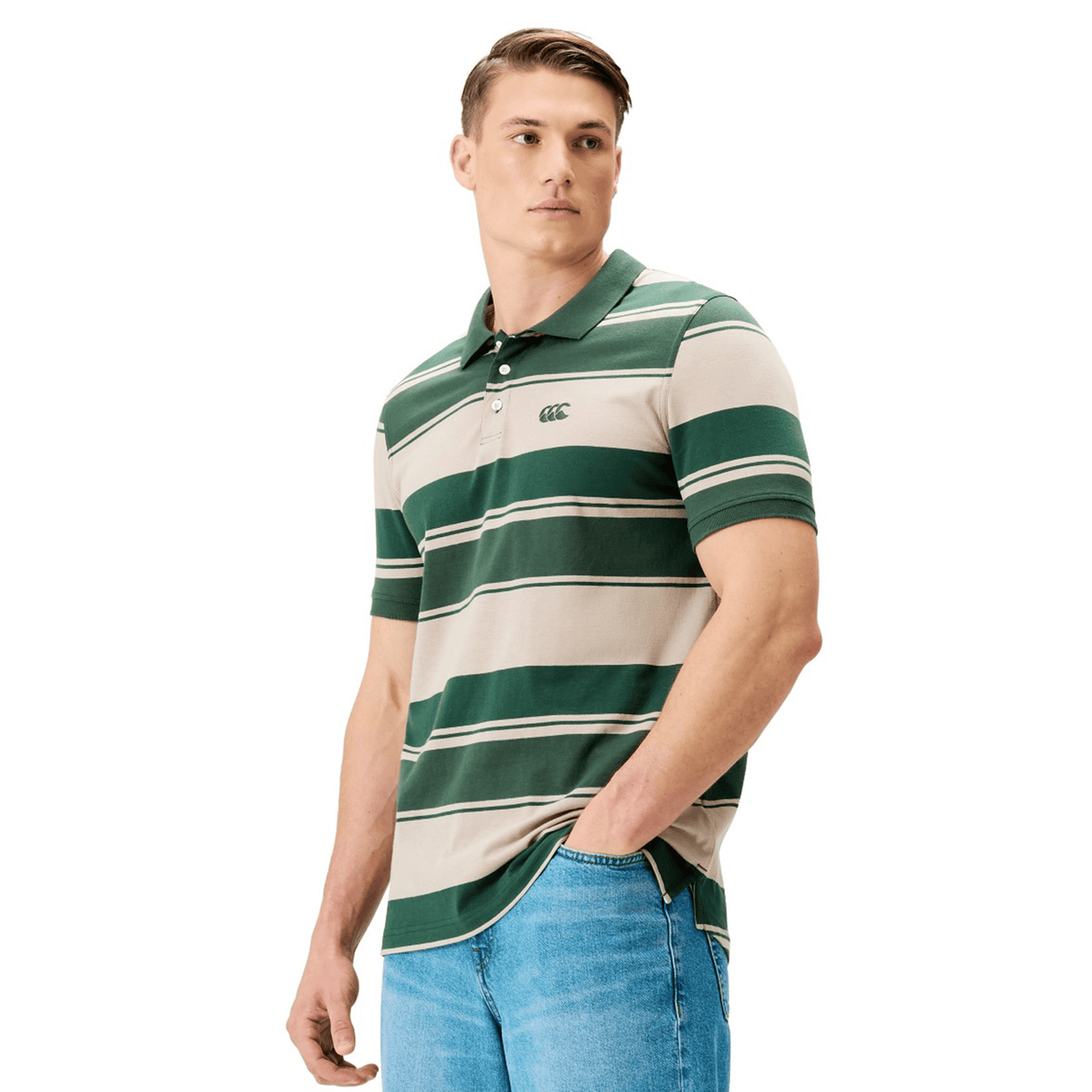 A man in a Canterbury Yarn Stripe Polo by Canterbury, featuring green and beige stripes, and blue jeans stands against a white background, highlighting classic rugby style.