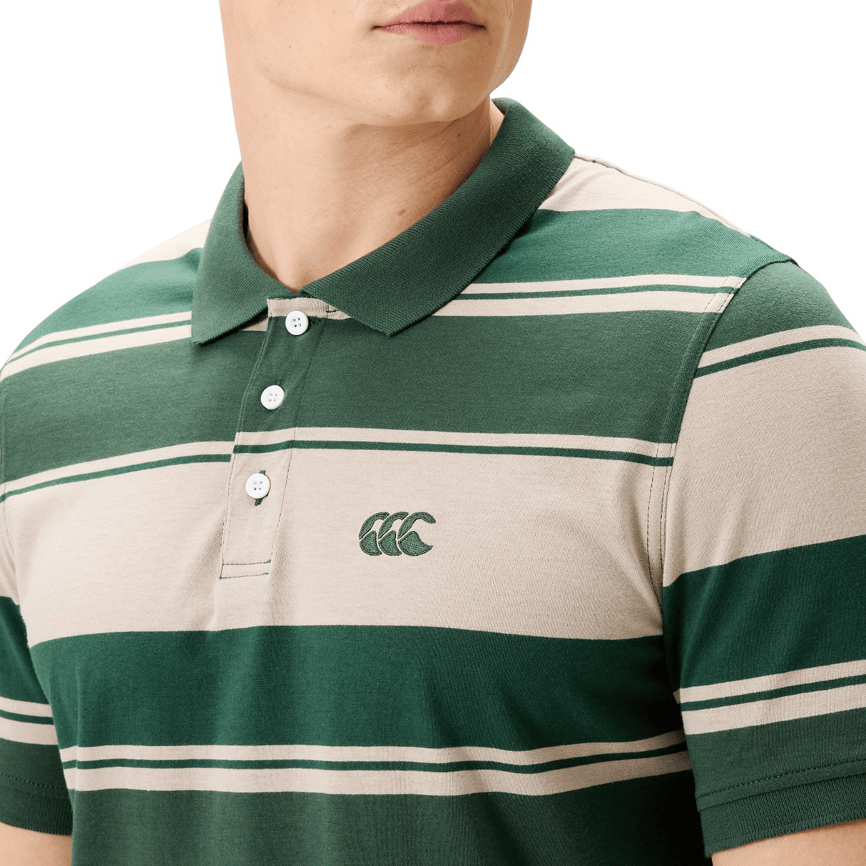 A person models the Canterbury Yarn Stripe Polo by Canterbury, a classic rugby-style shirt in green and beige with a collar, buttons, and an embroidered chest logo.