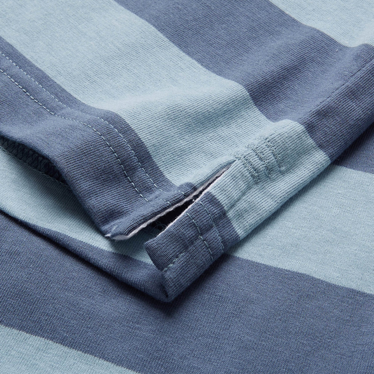 Close-up of the hem and side split on a Canterbury Yarn Stripe Polo by Canterbury, featuring blue and light blue striped fabric with detailed stitching and texture that emphasize its classic rugby-inspired style.