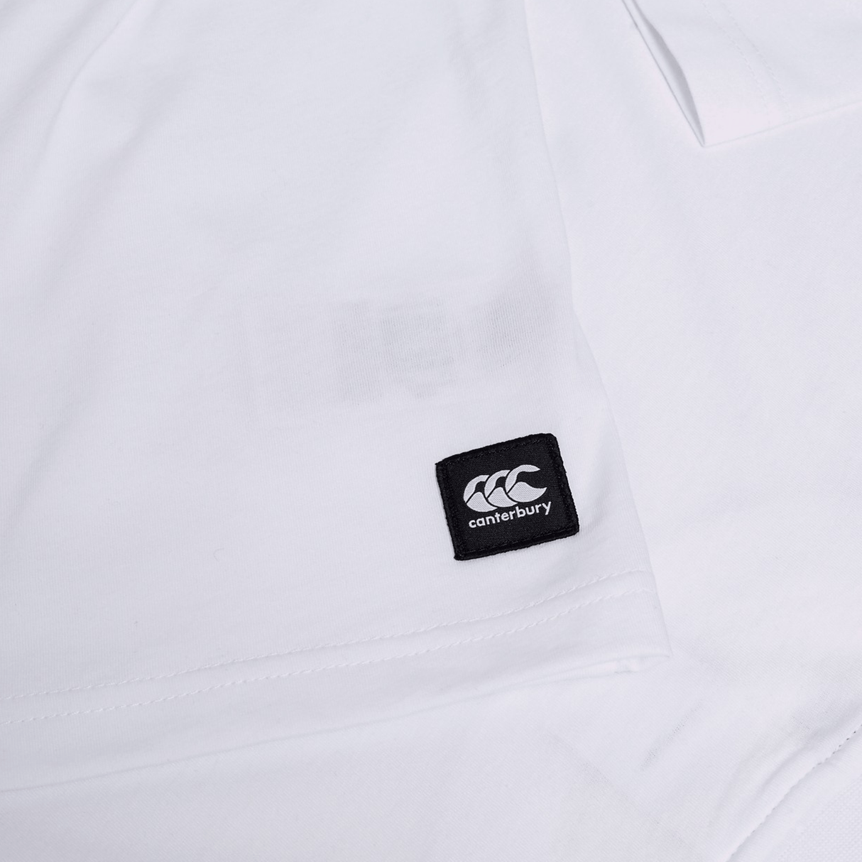 Close-up of the Canterbury Uglies Logo T-shirt in white, made from a cotton blend, featuring a small black square Canterbury label with white logo and text.