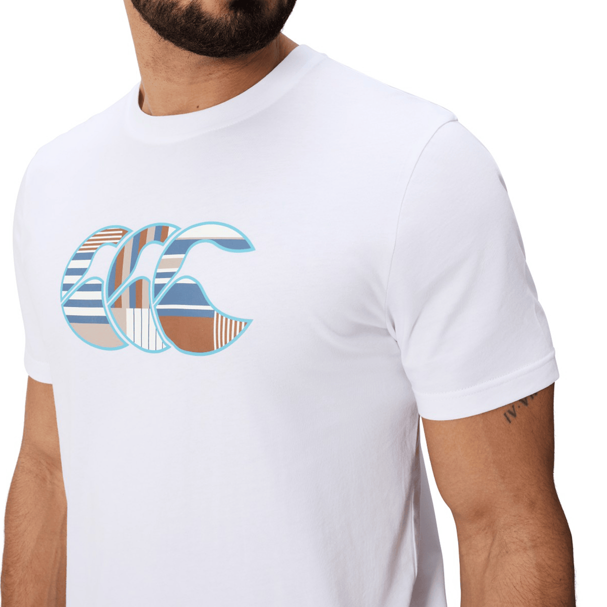 Man in a Canterbury Uglies Logo T-shirt by Canterbury, featuring a multicolored chest graphic and made from a white cotton blend, shows off a small upper arm tattoo.