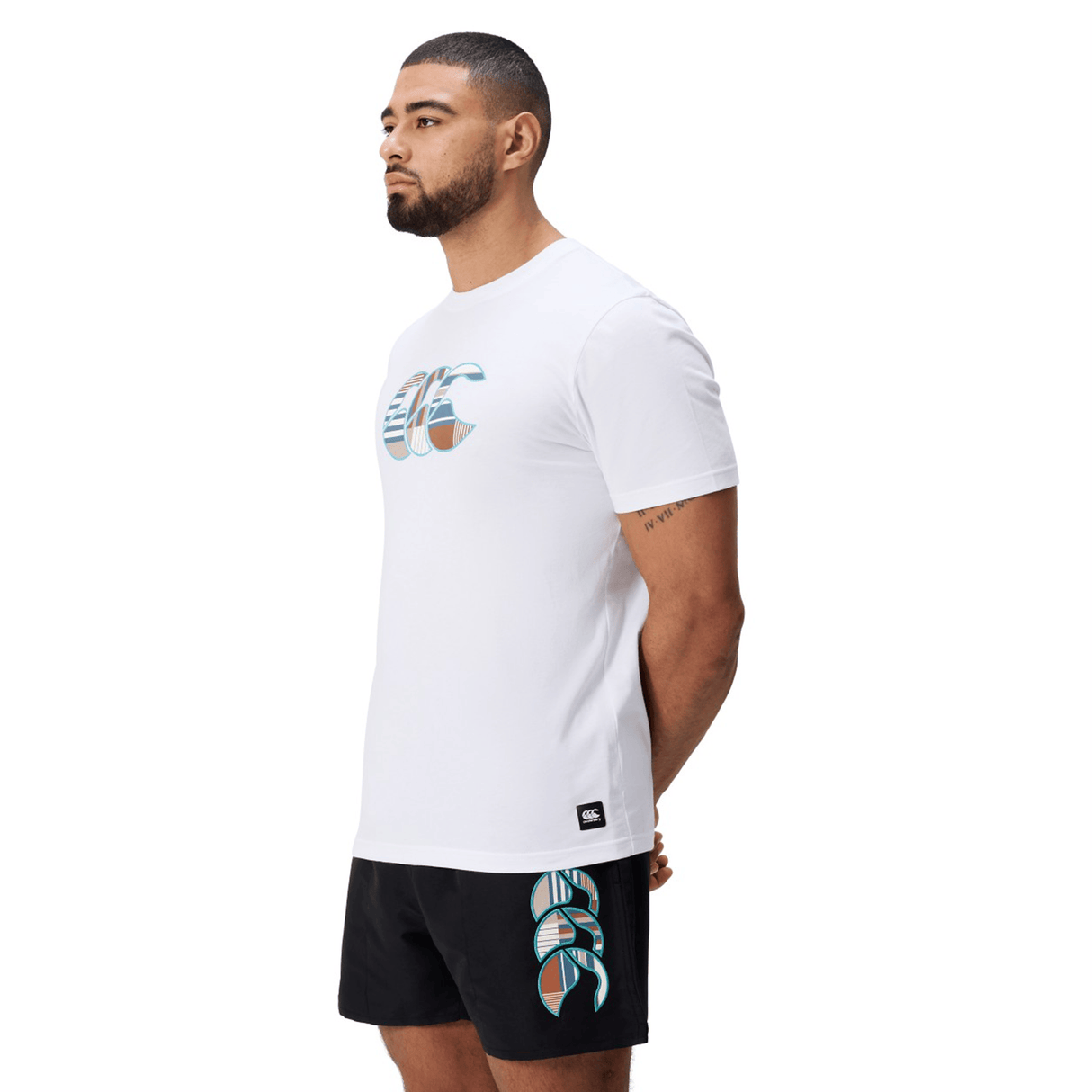 A man faces left, wearing a white Canterbury Uglies Logo T-shirt in a soft cotton blend and black shorts with matching graphics, set against a plain white background.