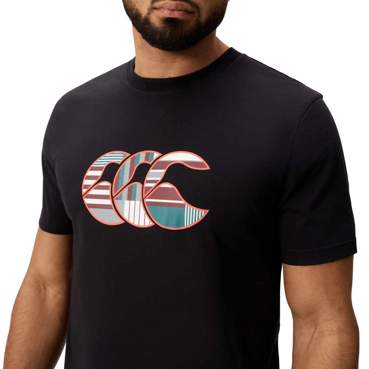 A man wearing the Canterbury Uglies Logo T-Shirt by Canterbury, a black cotton blend tee featuring a large, colorful graphic with overlapping curved shapes and striped patterns on the chest.