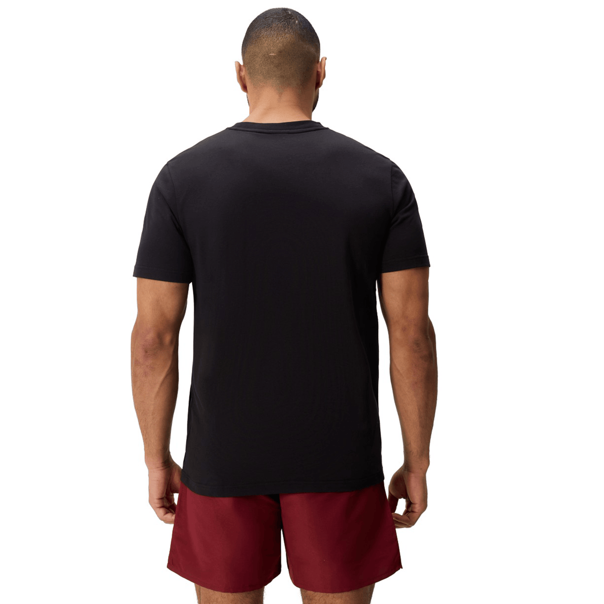 A person stands facing away from the camera, wearing a Canterbury Uglies Logo T-shirt by Canterbury and maroon shorts against a white background.