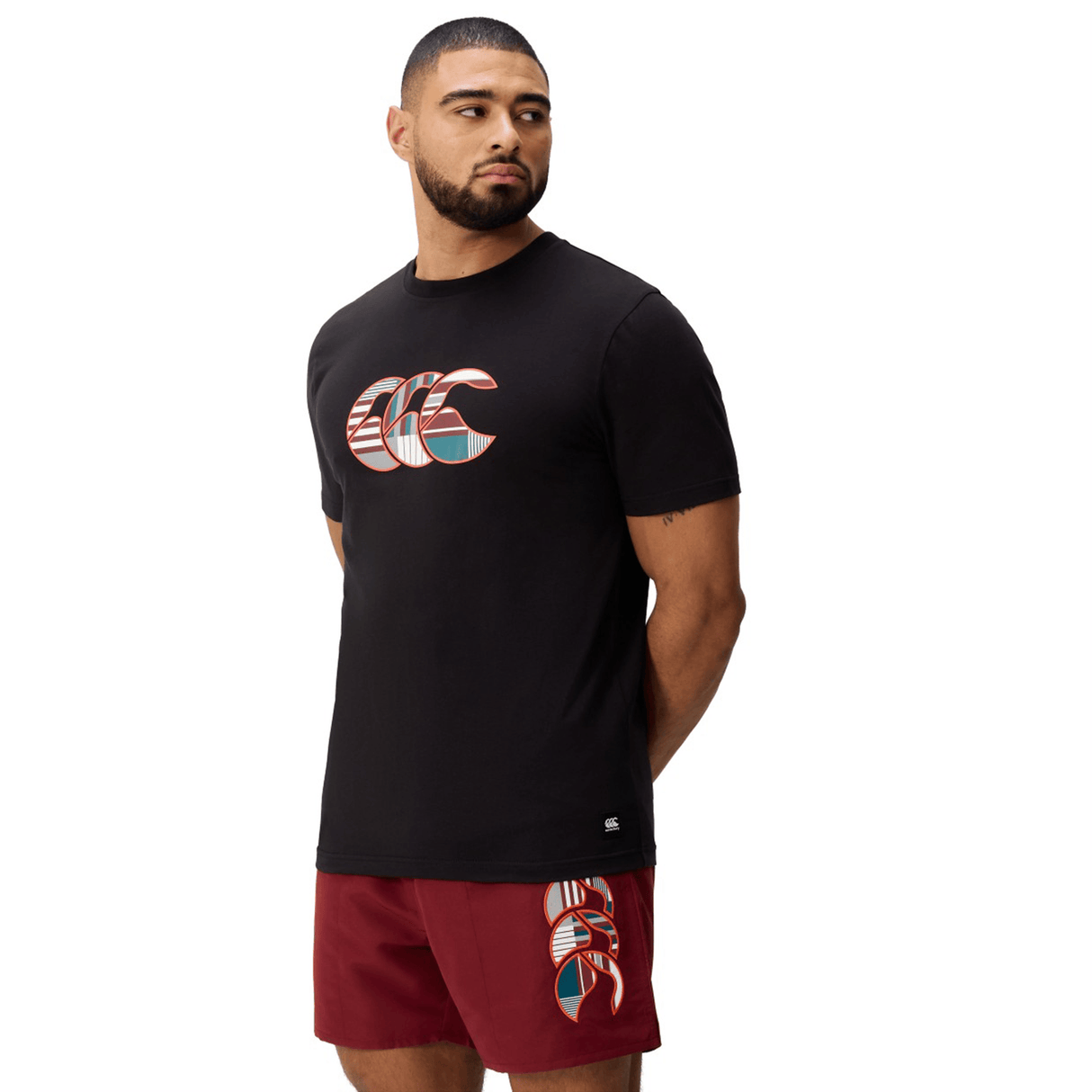 A man stands against a white background wearing Canterbury's Uglies Logo T-shirt in black cotton blend and matching maroon shorts, both featuring the distinctive Canterbury Uglies Logo design.