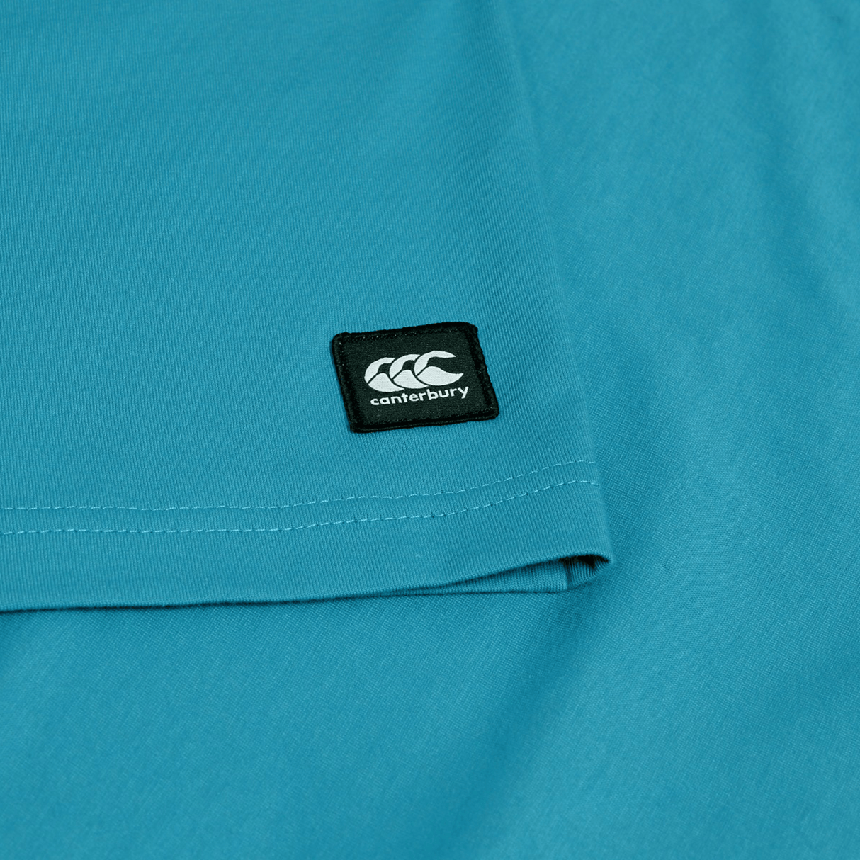 Close-up of the Canterbury Uglies Logo T-shirt, a teal cotton blend tee with a small black rectangular Canterbury patch displaying the white logo and text.