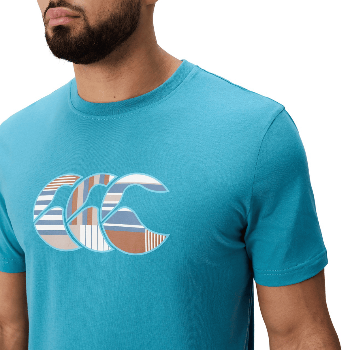 A man wears a Canterbury Uglies Logo T-shirt by Canterbury, featuring a turquoise cotton blend and striped graphic logo on the chest, shown from the shoulders up against a white background.