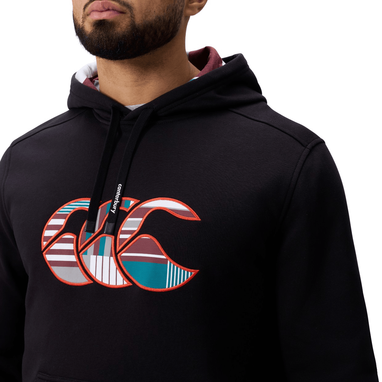 A person wearing a black Canterbury Uglies Logo Hoodie featuring a colorful logo and black drawstrings, shown from shoulders to chin.