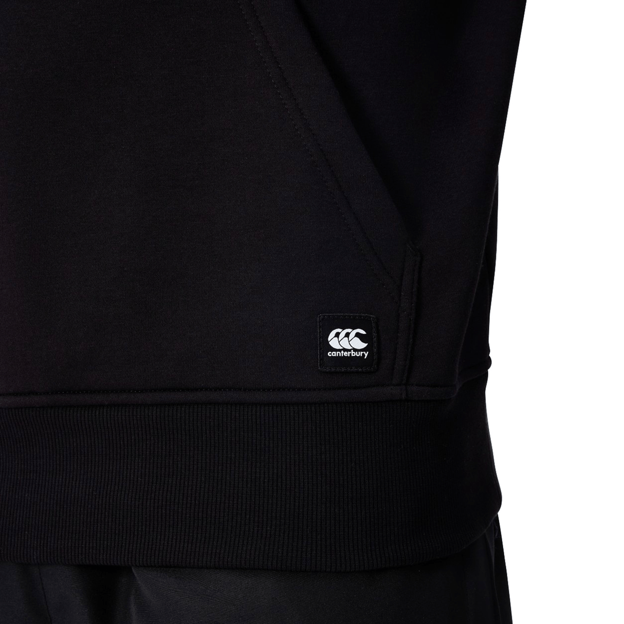 Close-up of the Canterbury Uglies Logo Hoodie by Canterbury, featuring a logo tag near the pocket, ribbed hem, and detailed pocket seam—ideal for rugby hoodie fans.