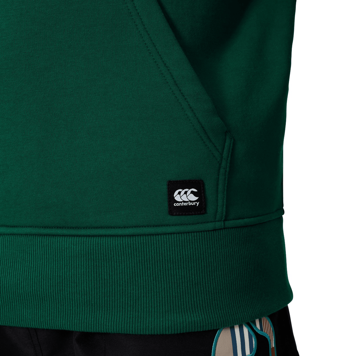Close-up of the Canterbury Uglies Logo Hoodie in green, featuring a black Canterbury logo tag near the hem and part of a pocket—ideal for classic rugby hoodie fans.