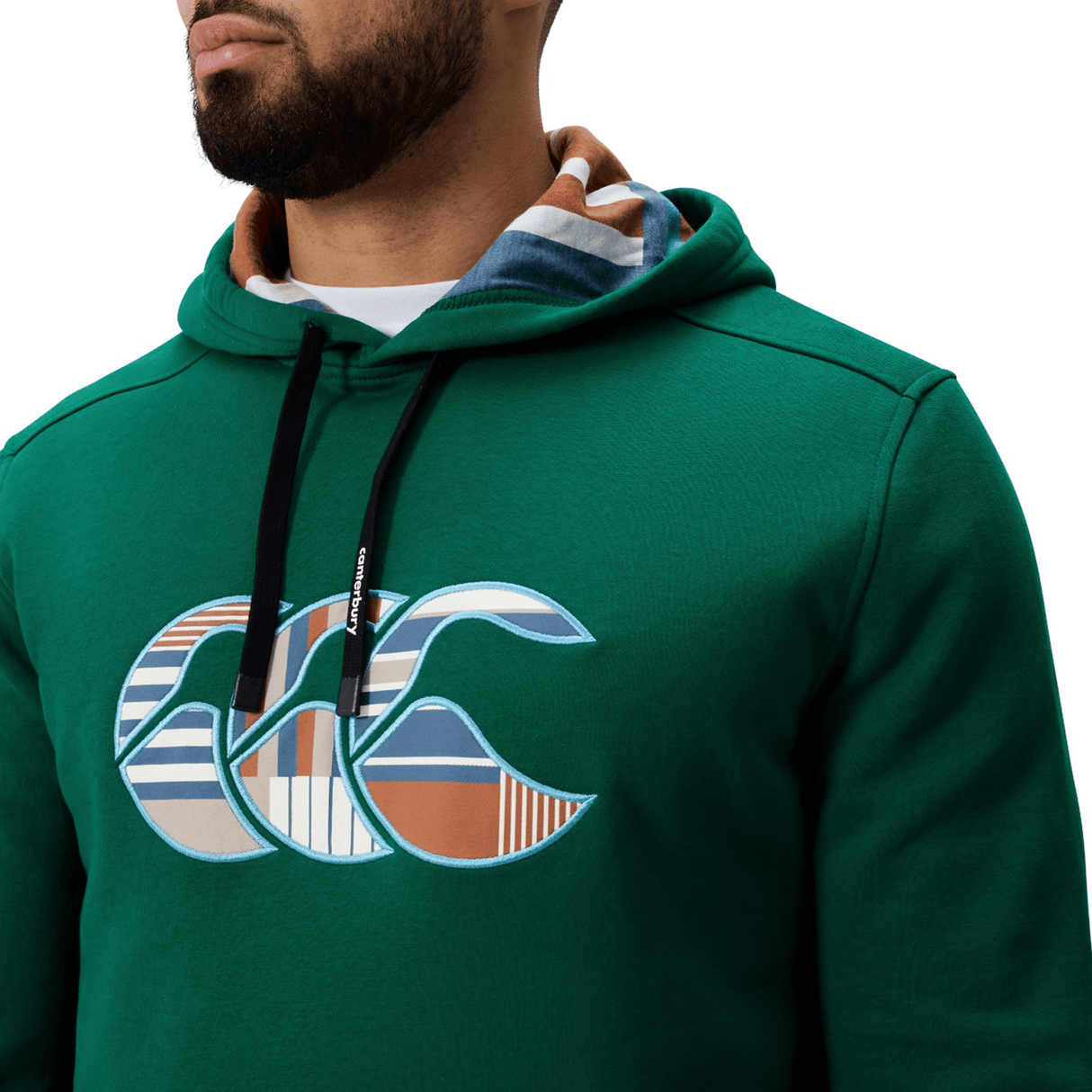 A man wears the Canterbury Uglies Logo Hoodie by Canterbury, featuring a green design, black drawstrings, and a multicolored patterned Uglies logo on the chest. Shown from the shoulders up.