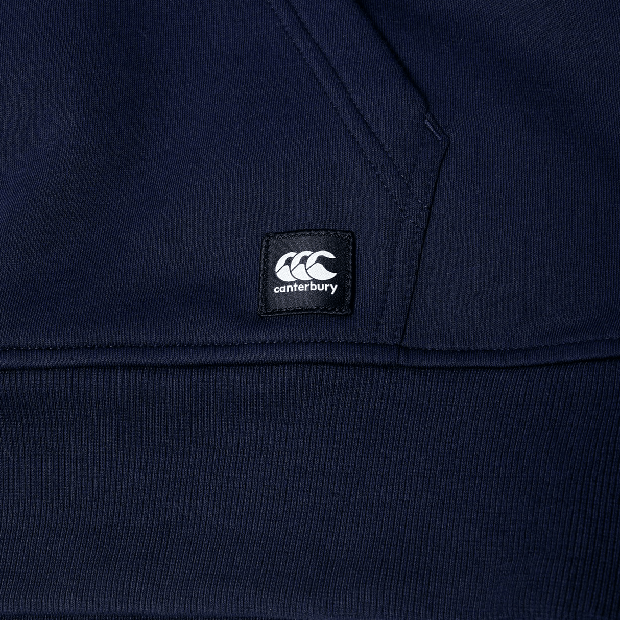 Close-up of a navy blue Canterbury Uglies Logo Hoodie, showcasing a visible pocket seam and a black Canterbury logo patch.