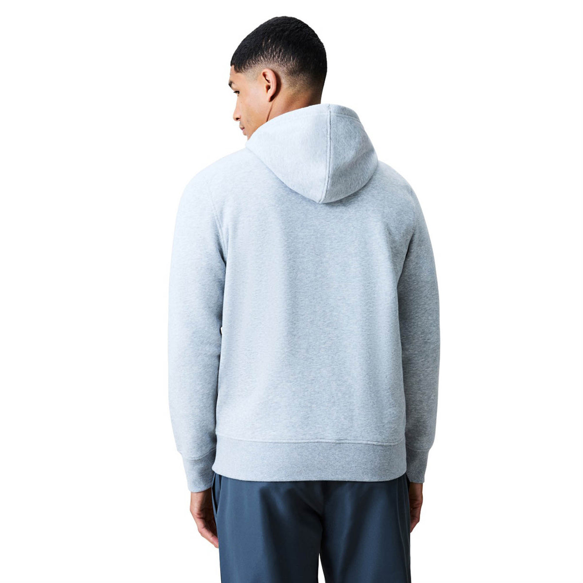 A man stands facing away, wearing a light gray Canterbury Uglies Logo Hoodie and dark pants, against a plain white background.