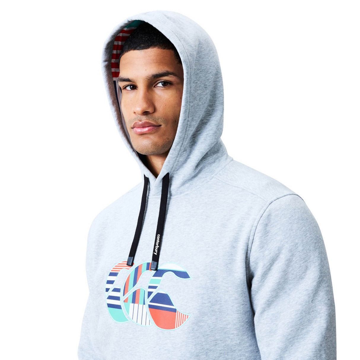 A man wearing the Canterbury Uglies Logo Hoodie in light gray, featuring a colorful Canterbury graphic on the chest and black drawstrings, looks at the camera against a white background.