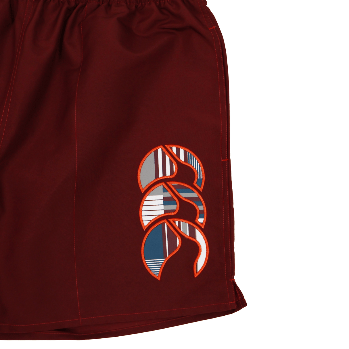A close-up of Canterbury Uglies 5" Tactic Shorts in maroon, featuring an abstract geometric logo in white, orange, navy, and gray on the left leg—durable training shorts ideal for any athlete.