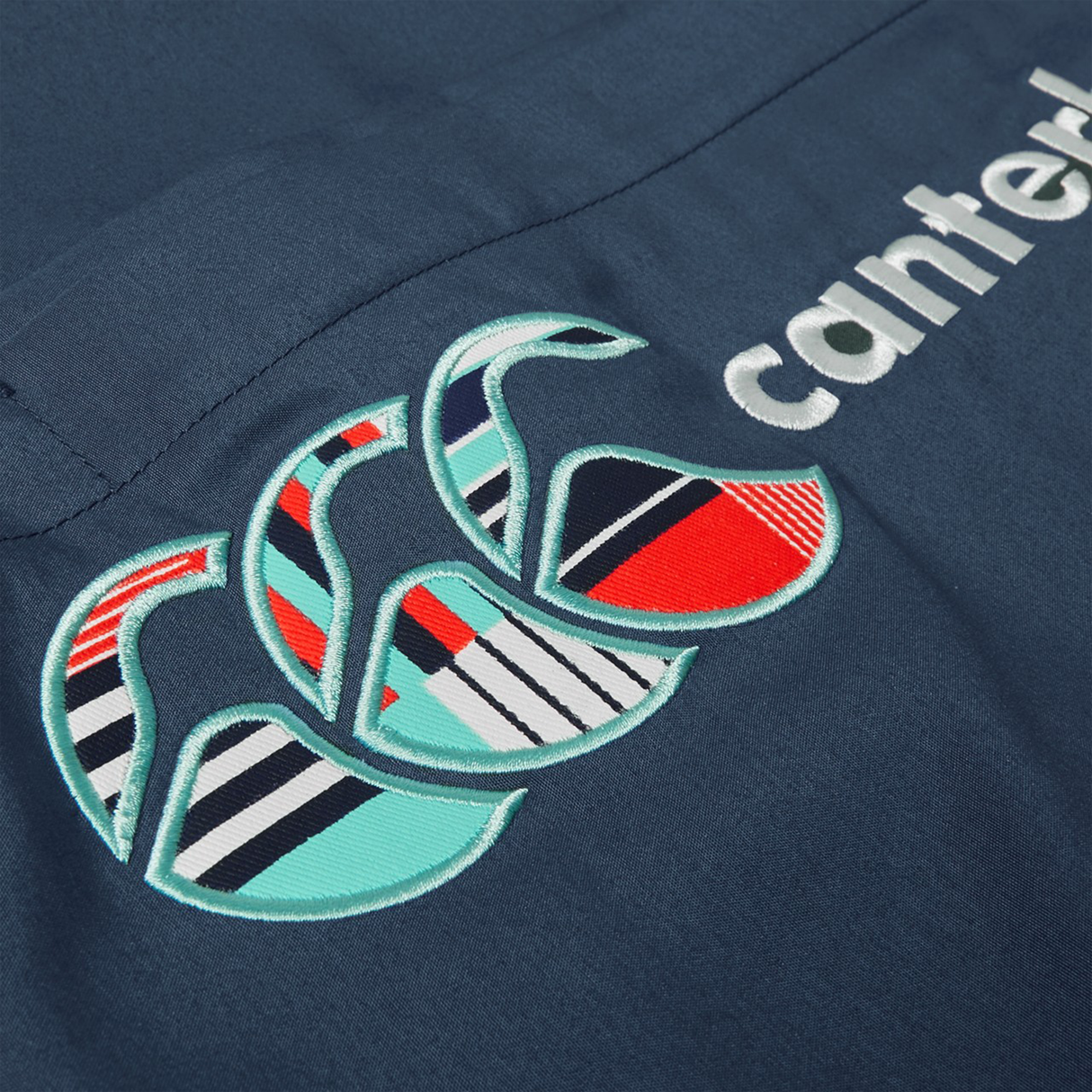 Close-up of navy Canterbury Uglies 32" Stadium Pant fabric featuring the embroidered Canterbury logo with three overlapping C's and part of "canterbury" in white.
