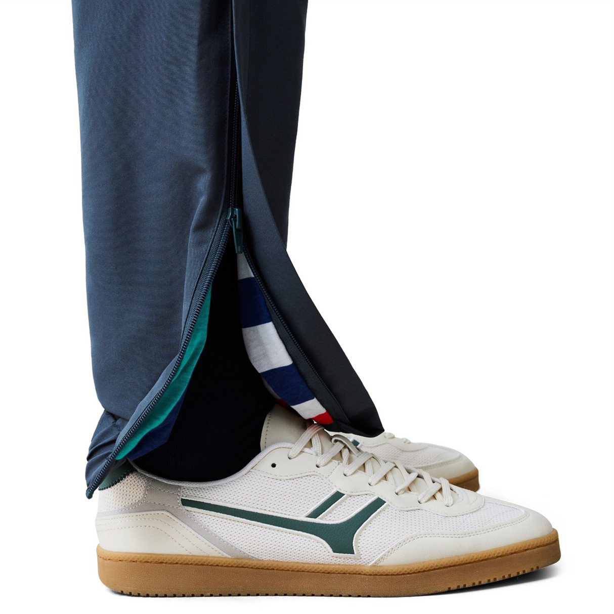 A person wearing Canterbury Uglies 32" Stadium Pants by Canterbury and white sneakers with green accents, standing on a white background.