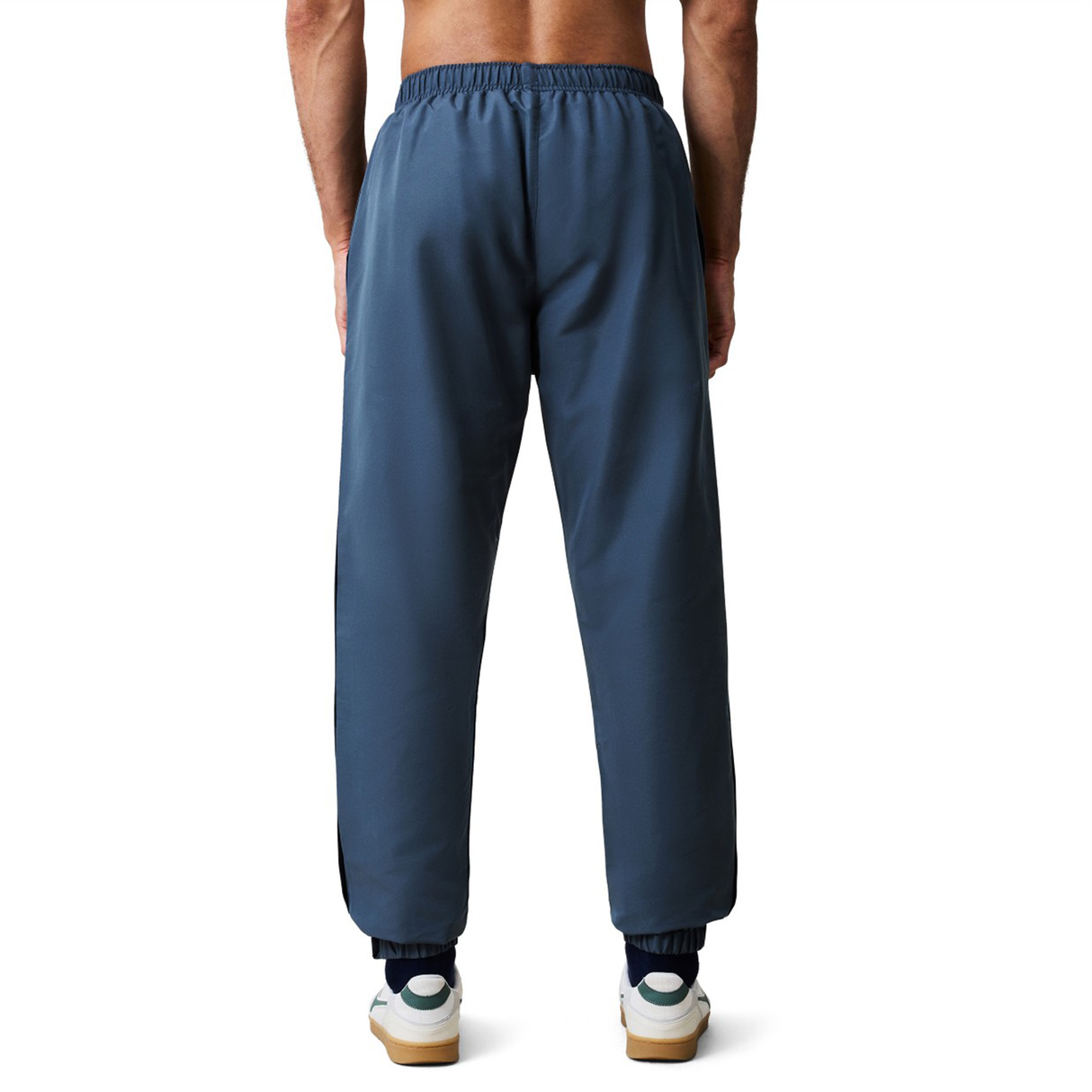 A person wearing blue Canterbury Uglies 32" Stadium Pant by Canterbury and white sneakers, viewed from behind against a plain white background.