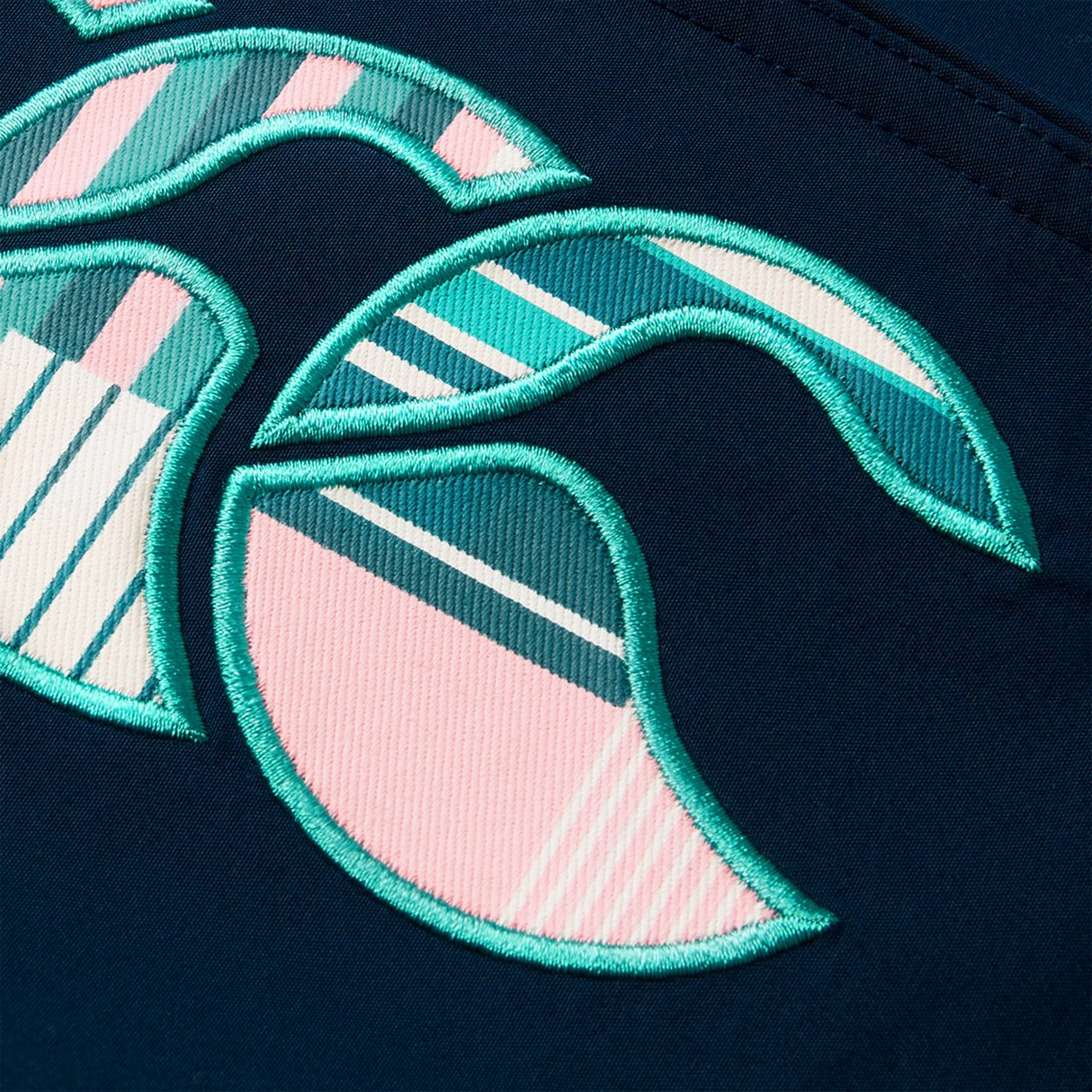 Abstract embroidery featuring teal, pink, and white curved and striped shapes on dark blue fabric, inspired by the vibrant patterns of Canterbury’s Women’s Canterbury Uglies Tactic Short.