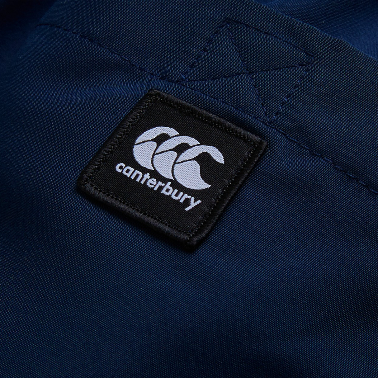 Close-up of a navy blue fabric with a black and white Canterbury logo patch stitched onto it, featured on the Women's Canterbury Uglies Tactic Short.