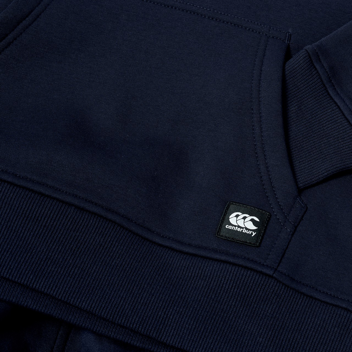 Close-up of the Canterbury Youth Uglies Logo Hoodie in navy blue, featuring a prominent Canterbury logo patch near the pocket and ribbed cuff detail, highlighting classic rugby style inspired by the iconic Canterbury Uglies collection.