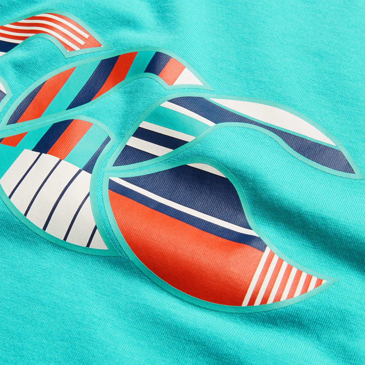 A close-up of the turquoise fabric from the Canterbury Youth Uglies Logo T-shirt, showcasing a graphic design with stylized waves in red, white, navy, and teal, highlighted by various stripe patterns.