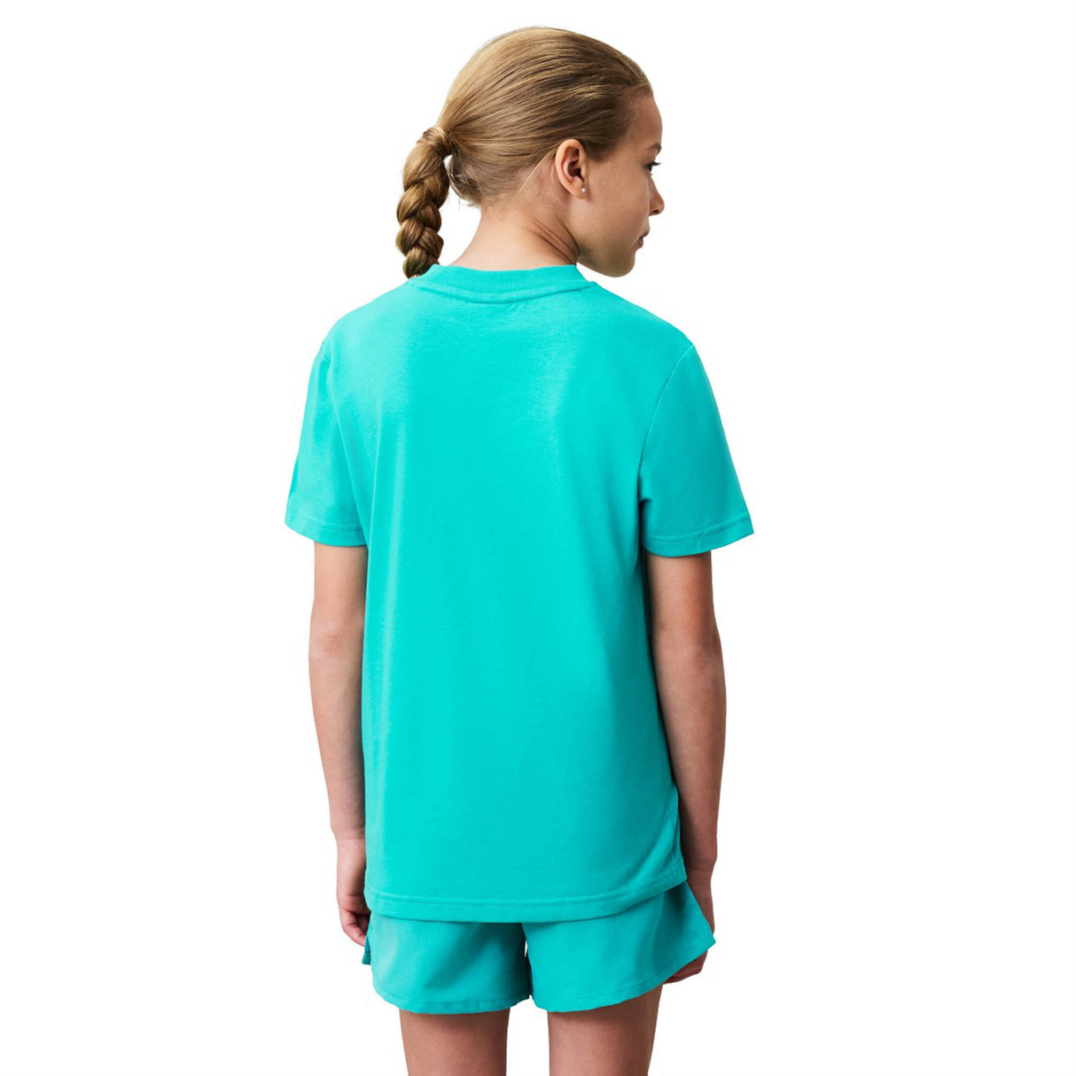 A young person with a braid stands facing away, wearing a matching turquoise Canterbury Youth Uglies Logo T-shirt and shorts against a white background.