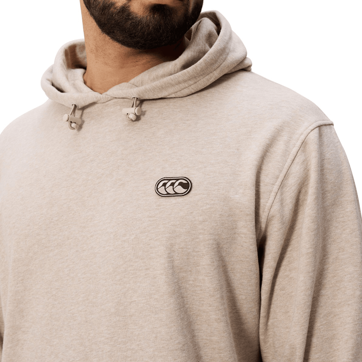 A man wearing the Canterbury FORCE HOODIE in beige, featuring a small embroidered chest logo, shown from the shoulders up.